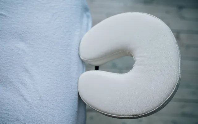 Une table de massage pliante noire installée dans un salon lumineux, avec serviettes et huiles.